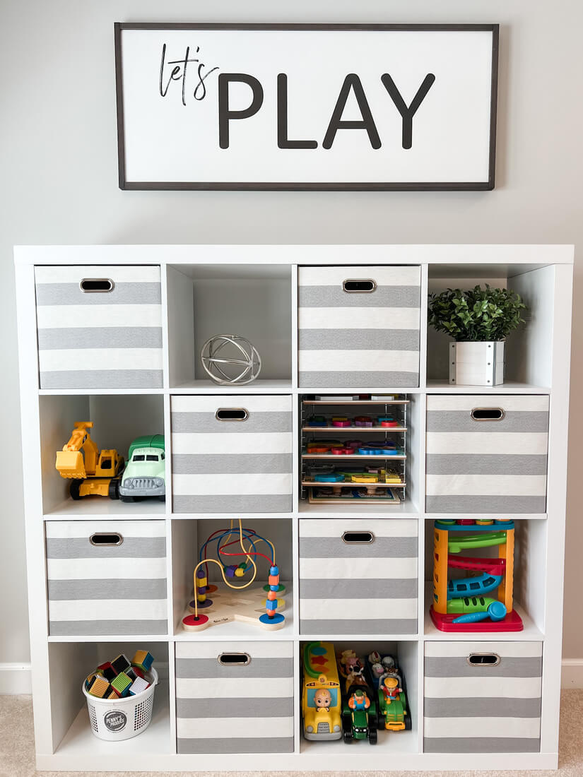 organized cube shelf in playroom with toys and let's play sign