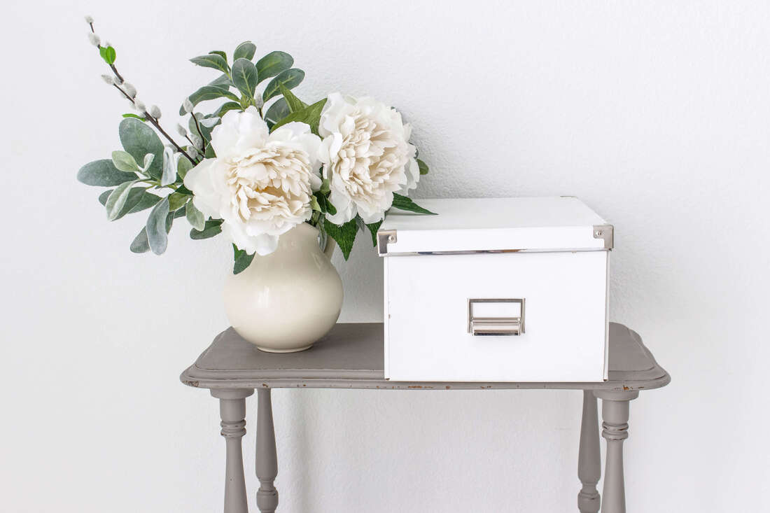 Grey entry table with white flower and memory box on top.