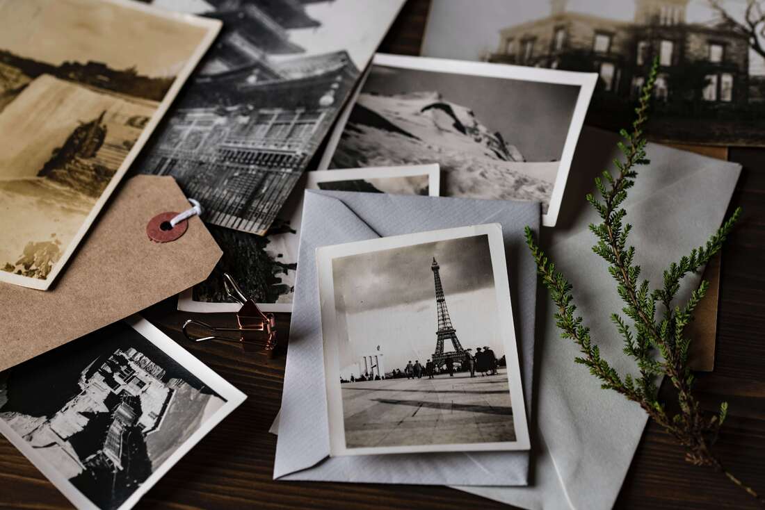 Vintage photos in pile on desk with Eiffel tower photo on top.