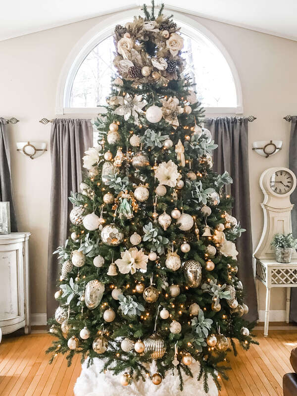 Tall decorated Christmas tree with white and gold ornaments and flowers.