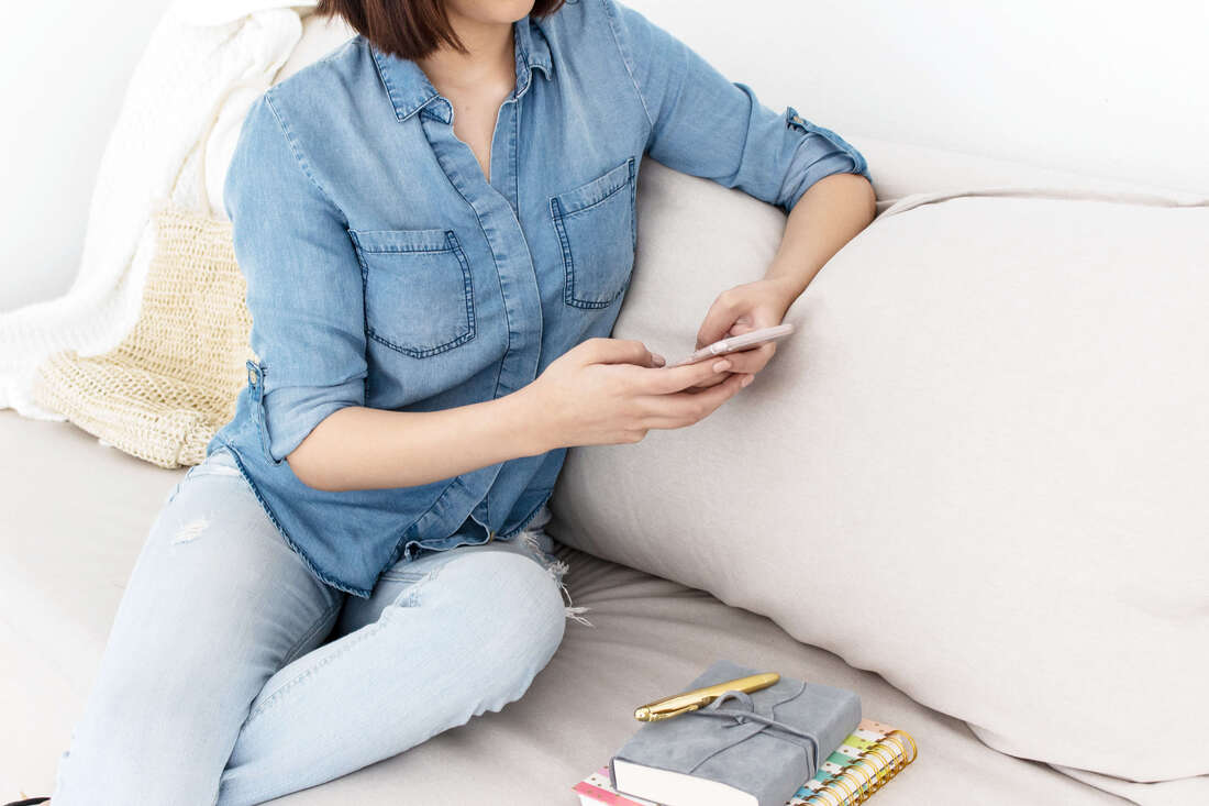 Women in denim shirt sitting on couch looking at phone.