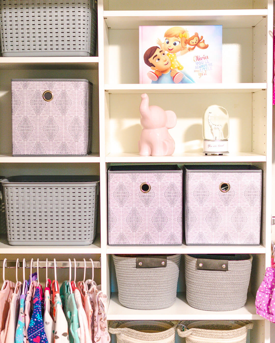 Girl white built in closet with gray baskets and pink elephant figurine.