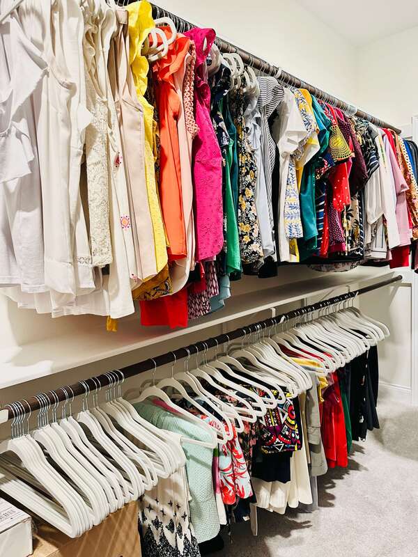 Walk in closet with two rows of colorful tops on bottom and pants below.