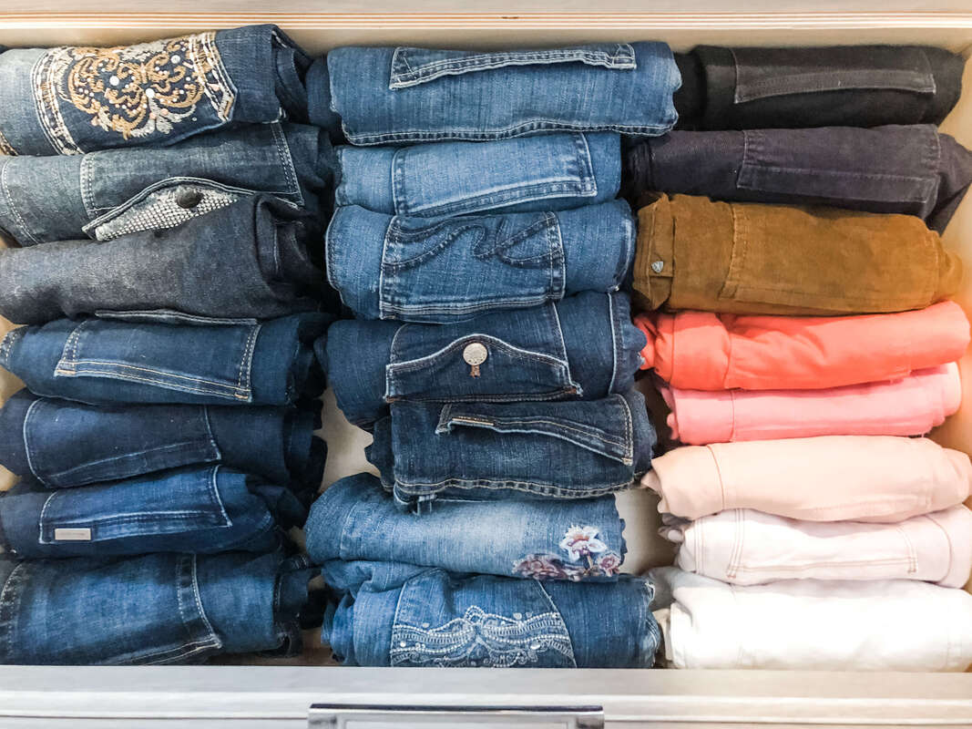 Two rows of jeans and one of pants folded vertically in drawer.