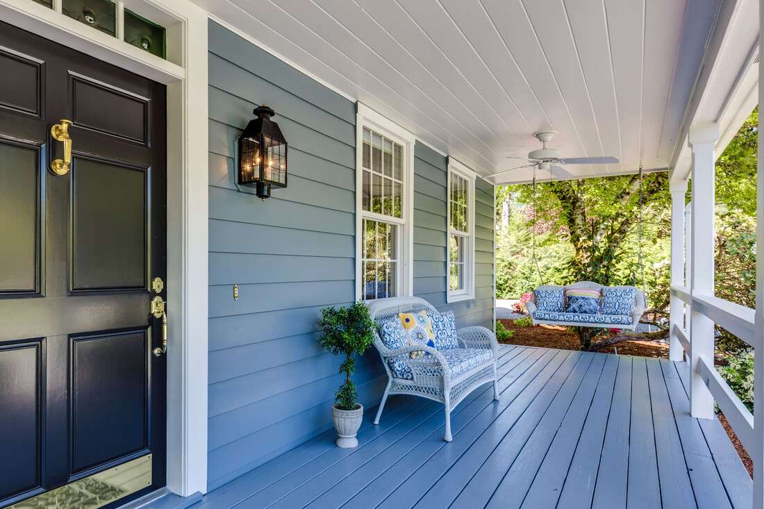 Front porch with blue swing and chair black front door and blue deck paint.