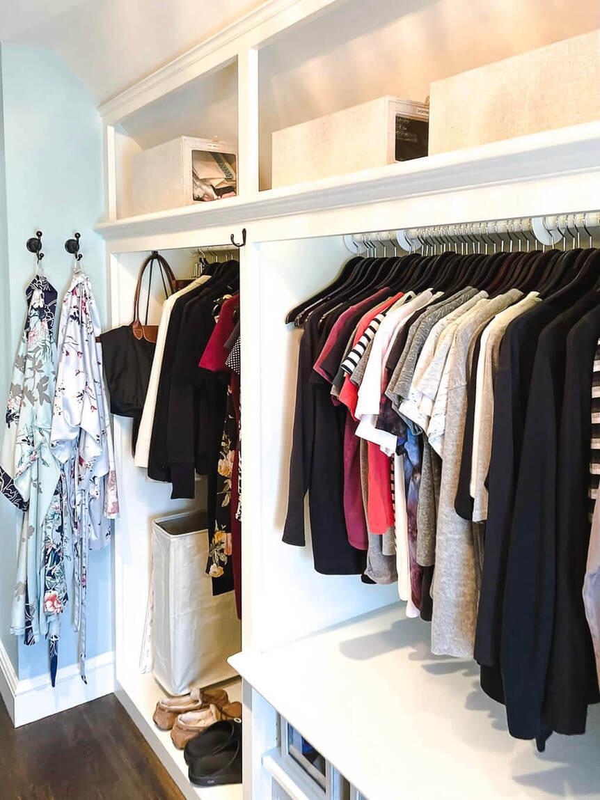 Walk in closet with two rows of colorful tops on bottom and pants below.